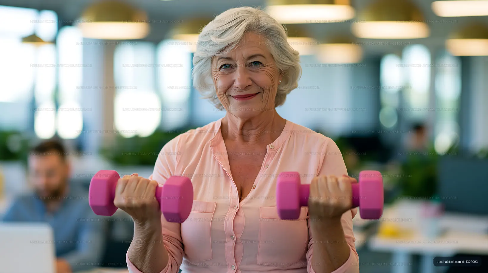 Senior woman exercising with pink dumbbells in modern office