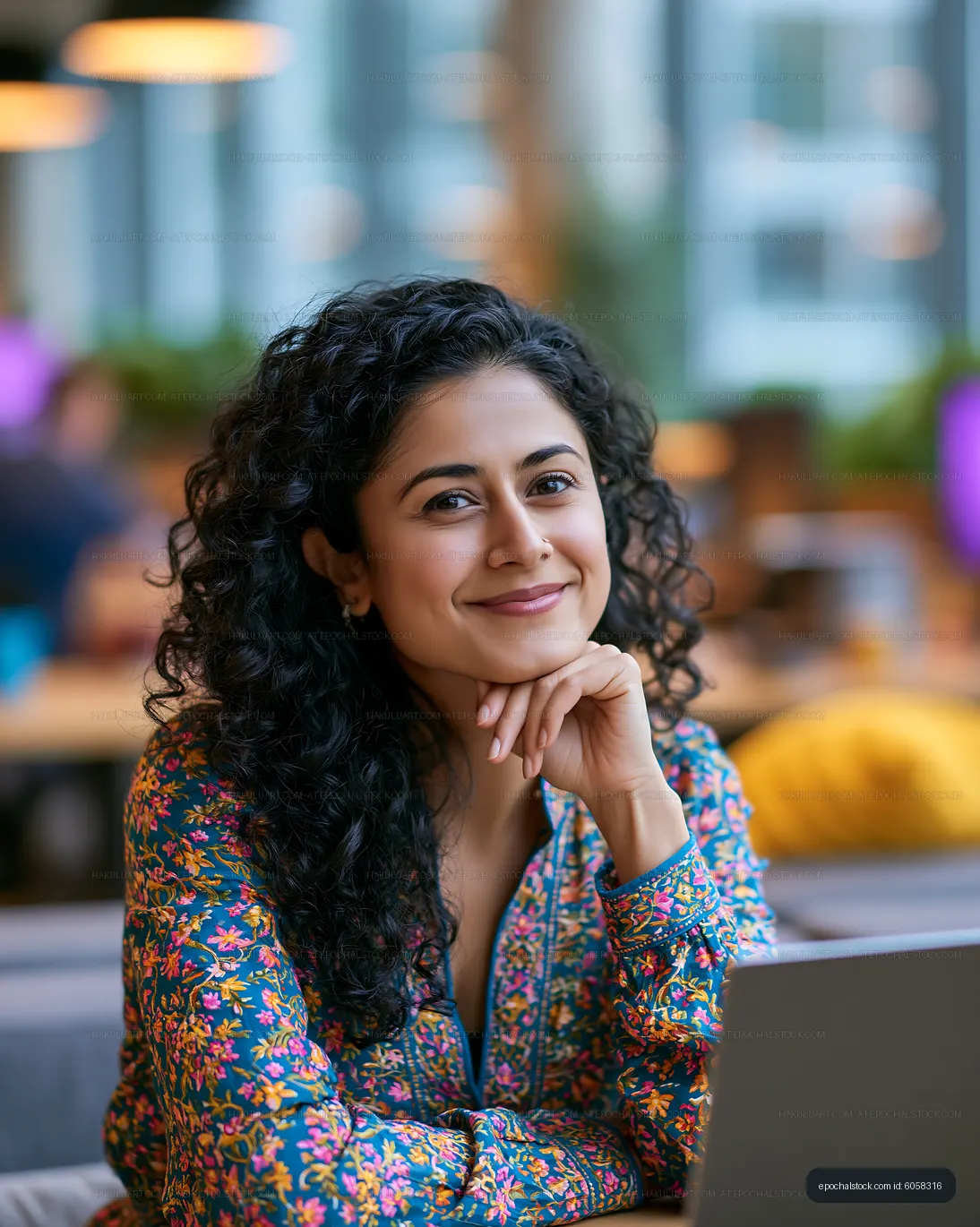 Woman with curly hair smiles while working on a laptop