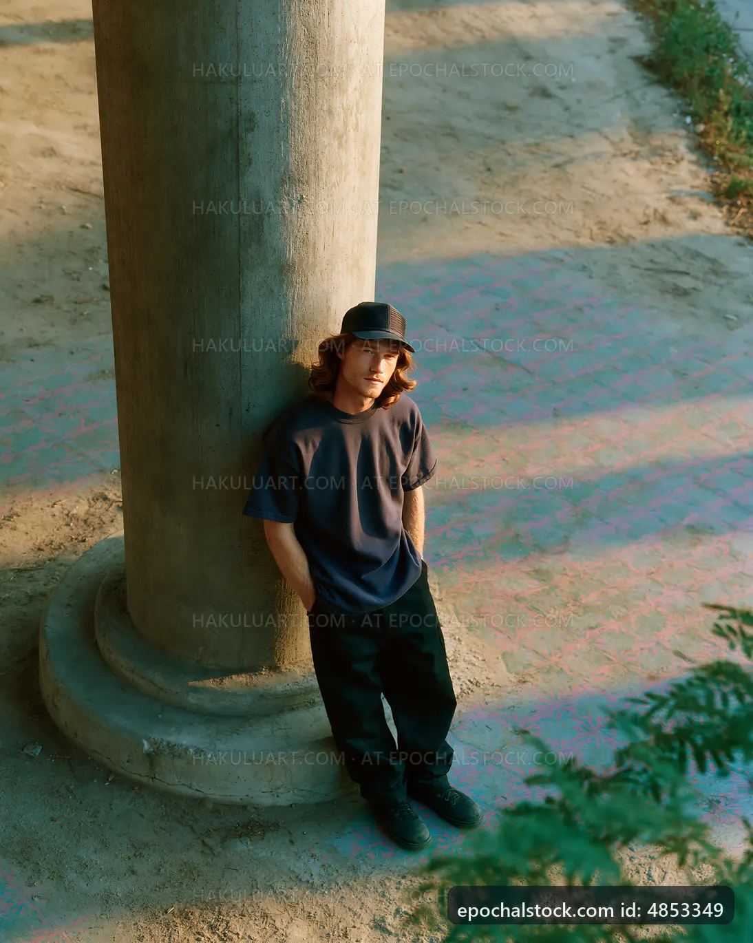 Man leaning against a pillar in outdoor setting during sunlight