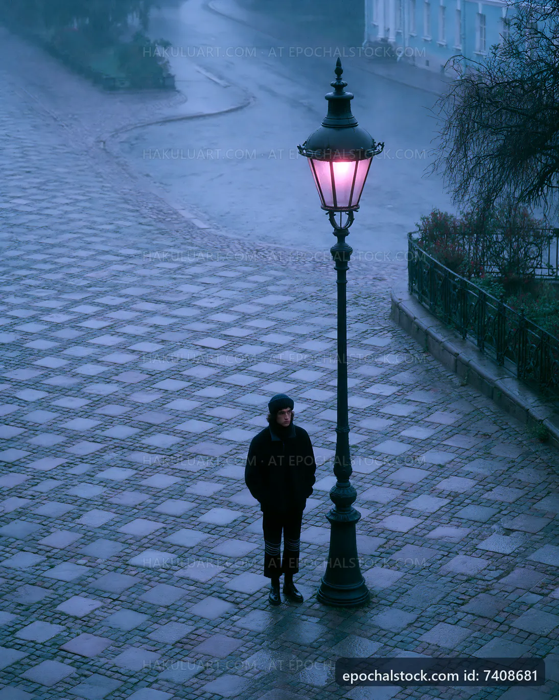 Person standing under street lamp in a rainy town square