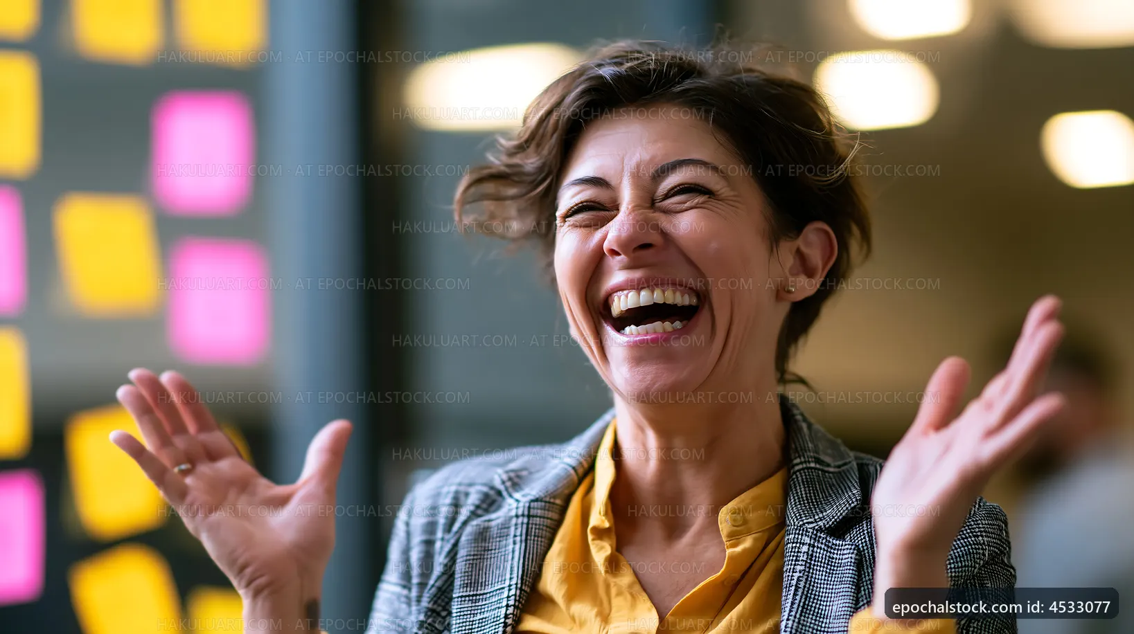 Woman laughing in an office setting with sticky notes on a wall