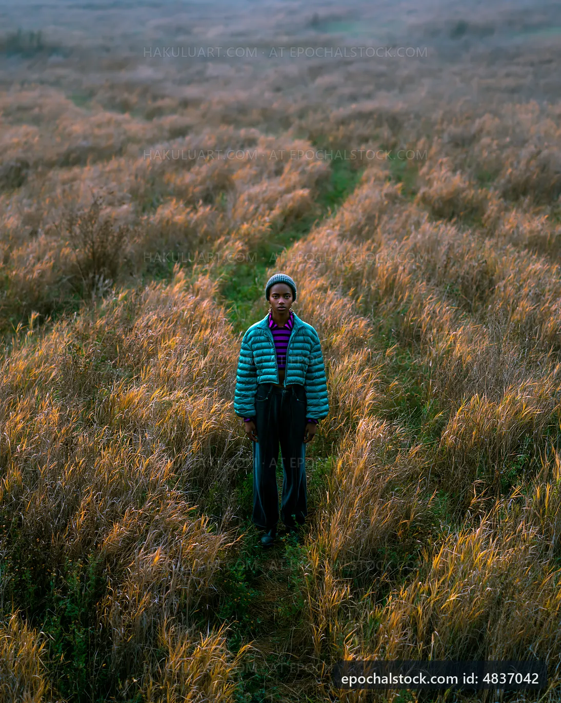 Person standing in tall grass field at sunset