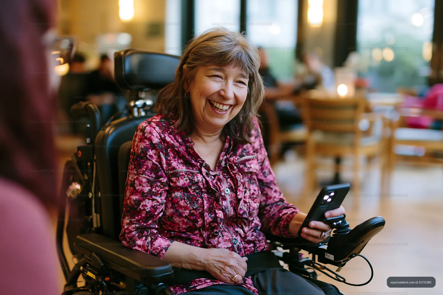 Woman in wheelchair smiling while using smartphone in cafe setting