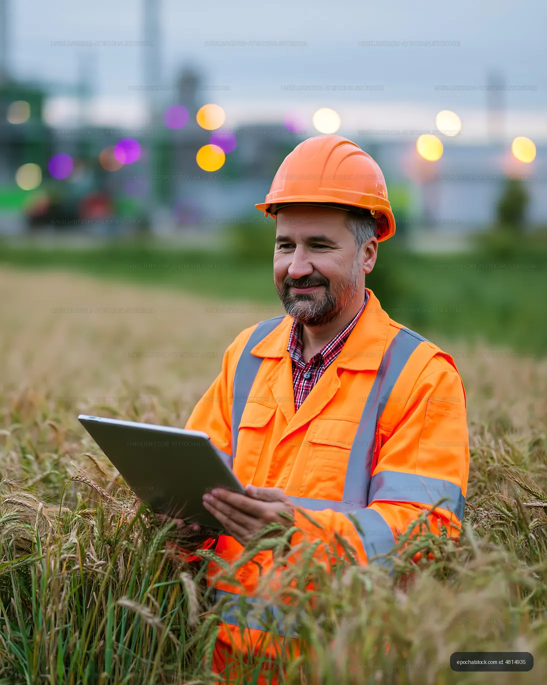 Man in orange safety gear using tablet in wheat field at dusk