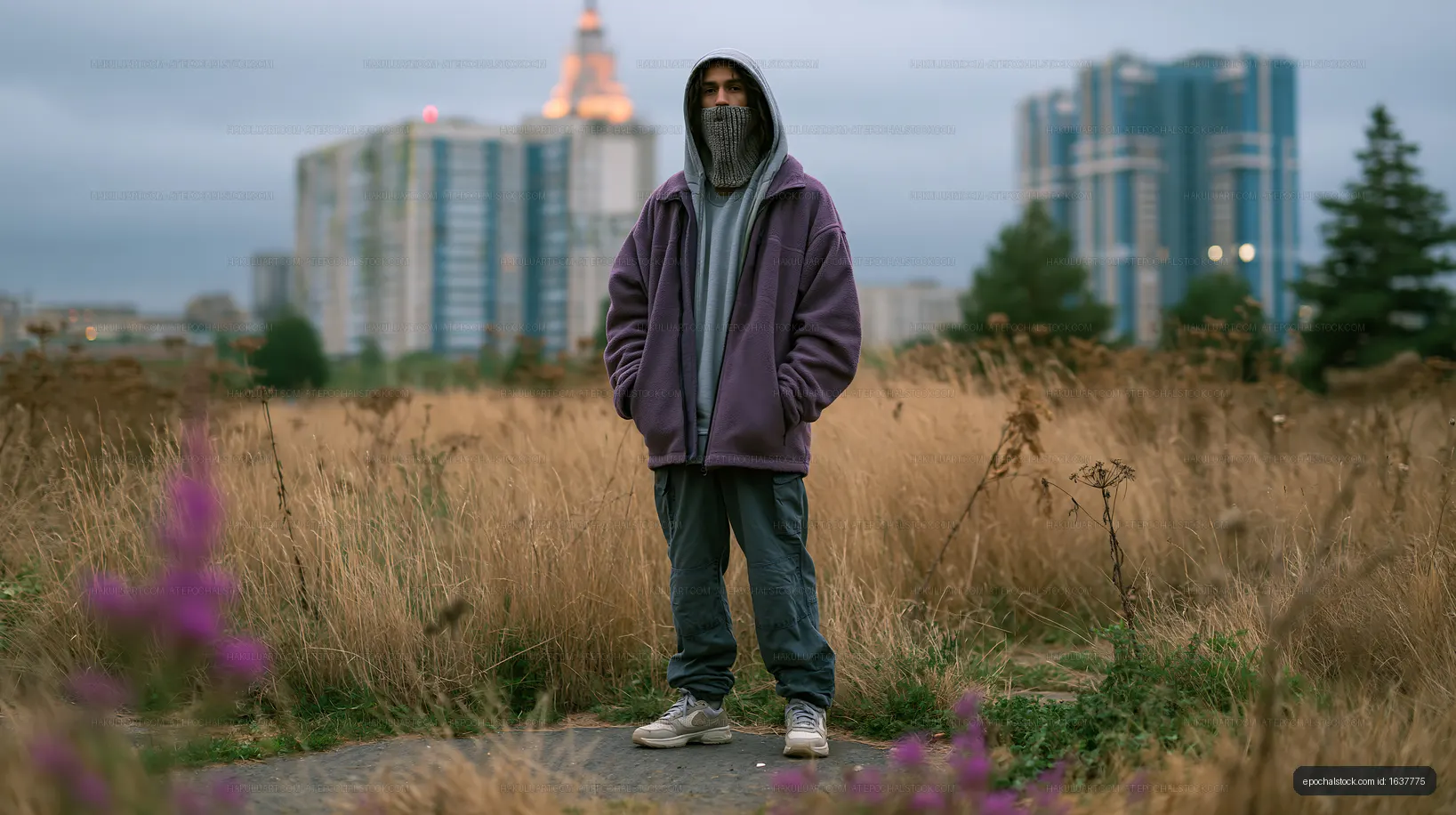 Person in hoodie standing in a field with city buildings in background