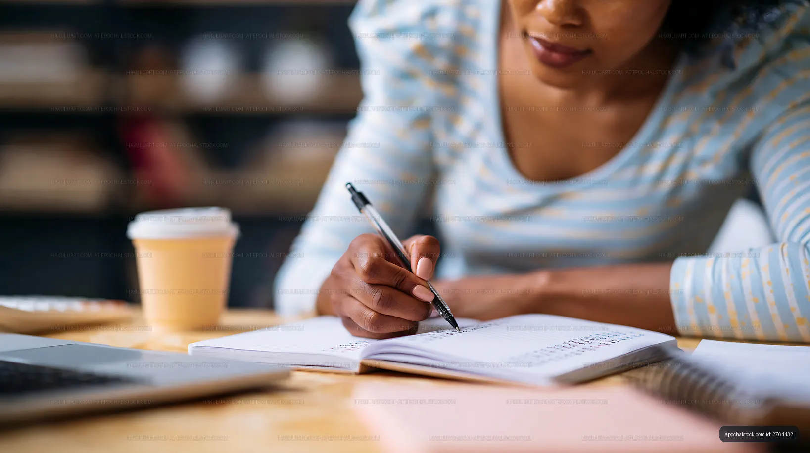 Woman writing in notebook at a desk with laptop and coffee
