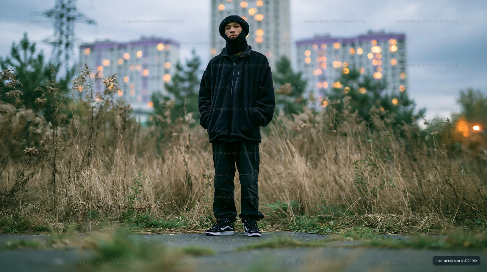 Person standing in field near urban buildings at dusk