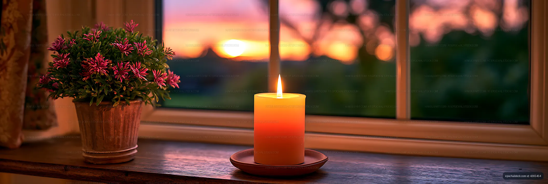 Lit pillar candle and potted flowers against a sunset view