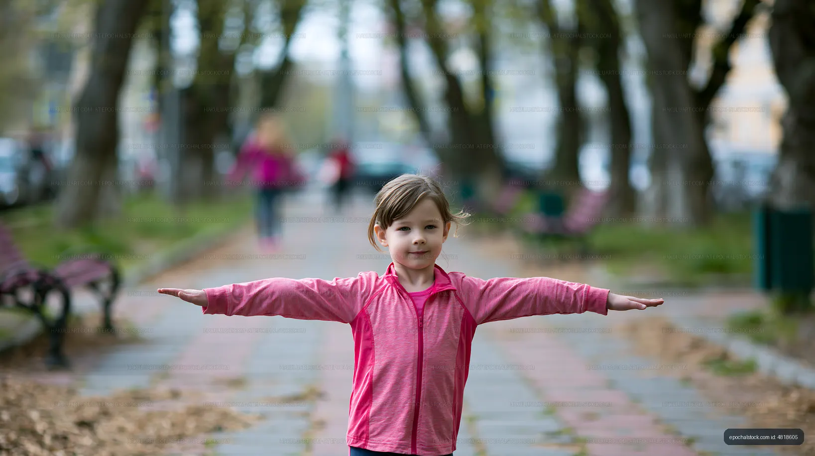 Child posing with outstretched arms on a park walkway