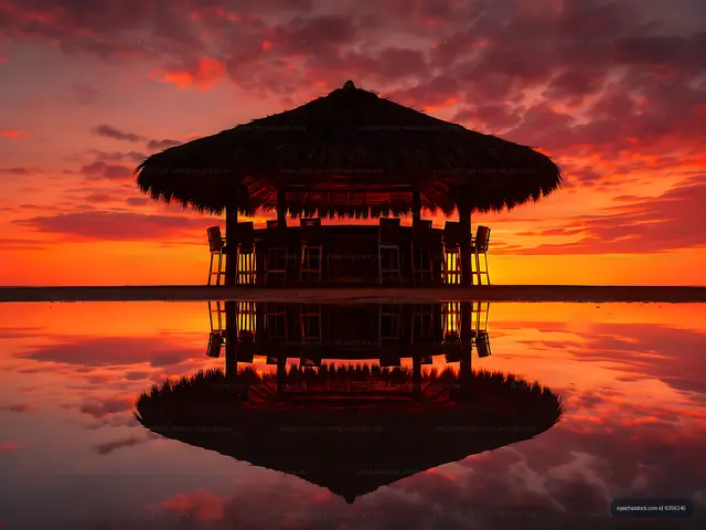 Sunset over beach hut with reflection in calm water