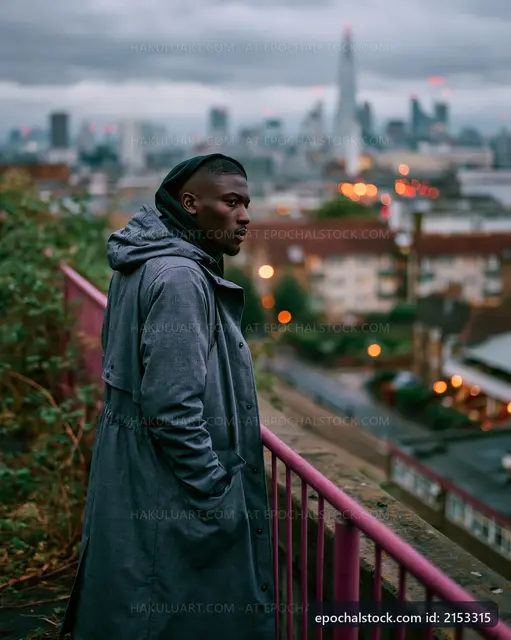 Man in gray coat looking over city skyline at dusk