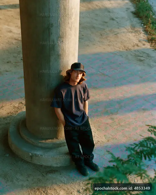 Man leaning against a pillar in outdoor setting during sunlight