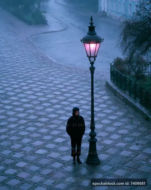 Person standing under street lamp in a rainy town square