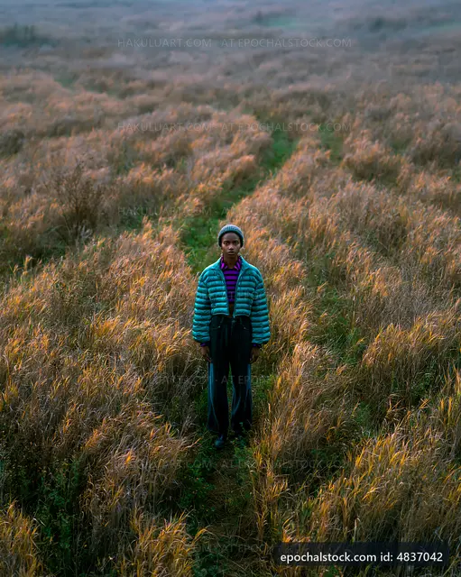 Person standing in tall grass field at sunset