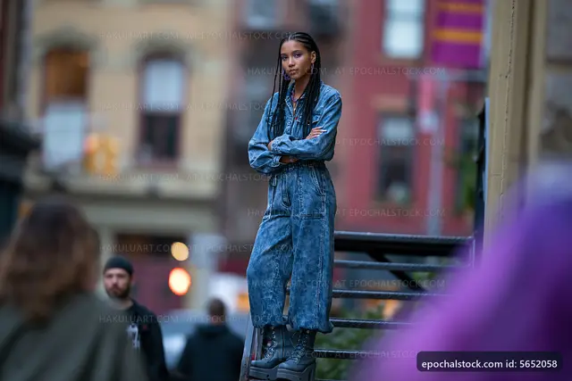 Young woman in denim jumpsuit standing on staircase in city street