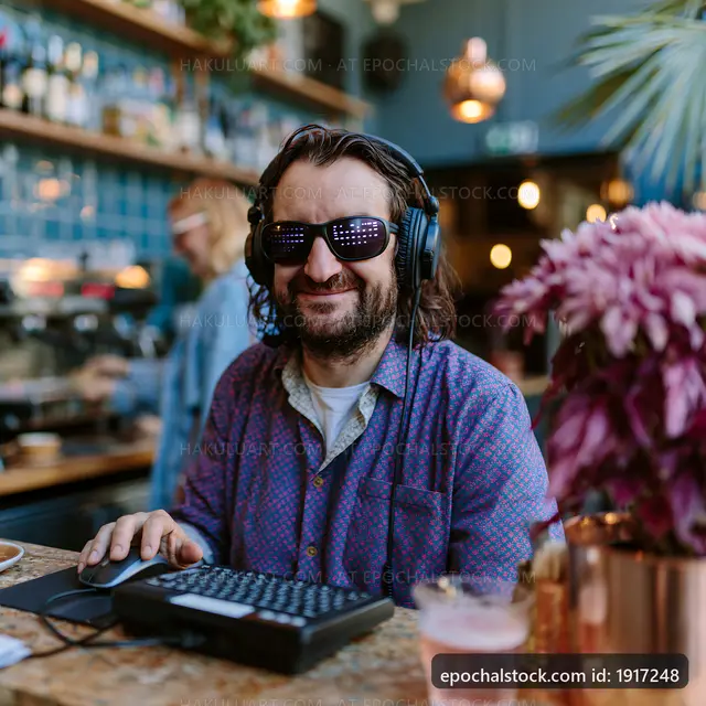 Man working on a computer in a cafe with headphones and sunglasses
