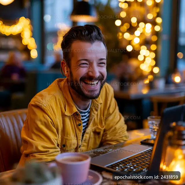 Man smiles while working on a laptop in a cozy cafe