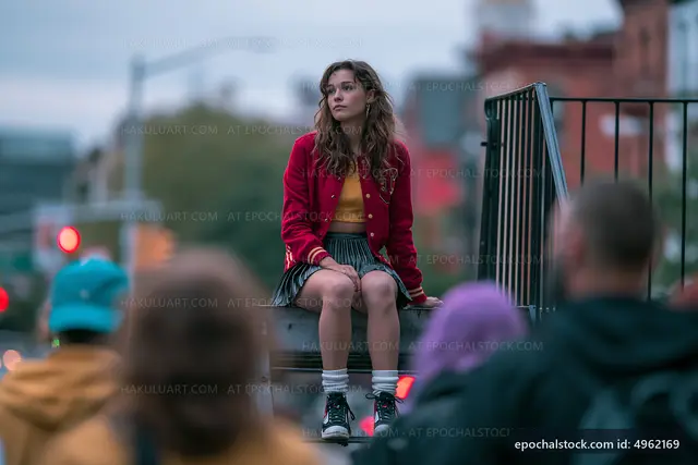 Teen girl sitting on a railing in urban setting with crowd below
