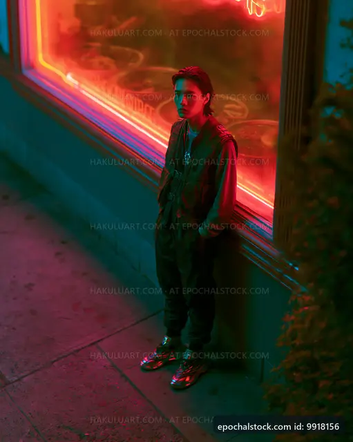 Young person standing near a neon-lit window at night