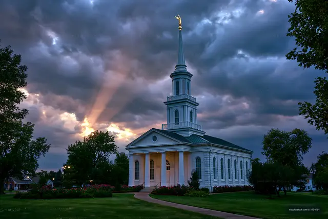 Church building with tall spire under dramatic sky at sunset