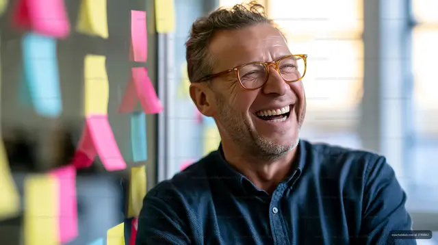 Man smiles in office with colorful sticky notes on wall