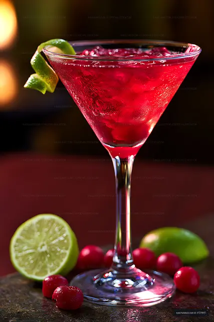Red martini cocktail surrounded by lime and cranberries