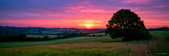 Panoramic rural fields beneath a vivid pink sunset sky